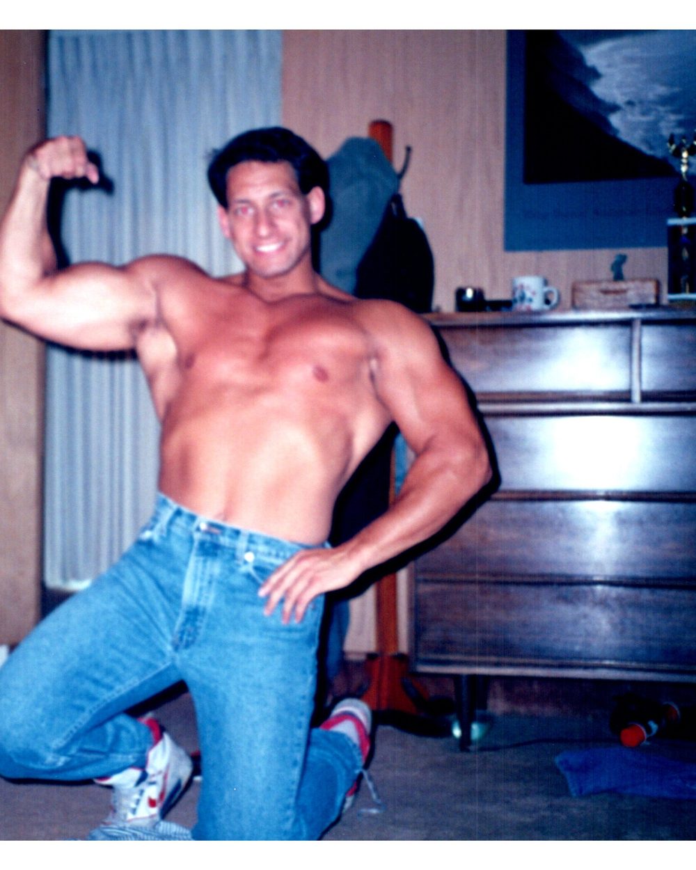 A young Ben flexing one arm in a bedroom, wearing jeans