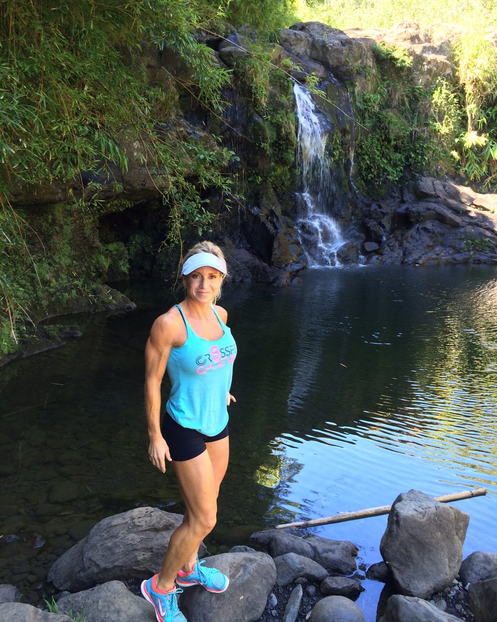 Loree standing on rocks at the edge of a pool below a waterfall in Hawaii