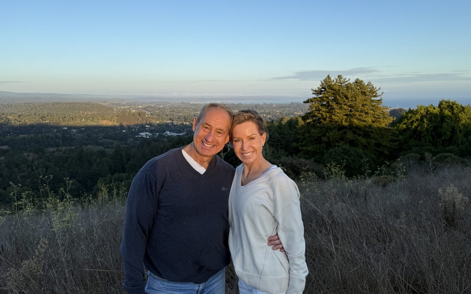 Ben and Loree standing together on a Santa Cruz hilltop at dusk with the valley lights behind them
