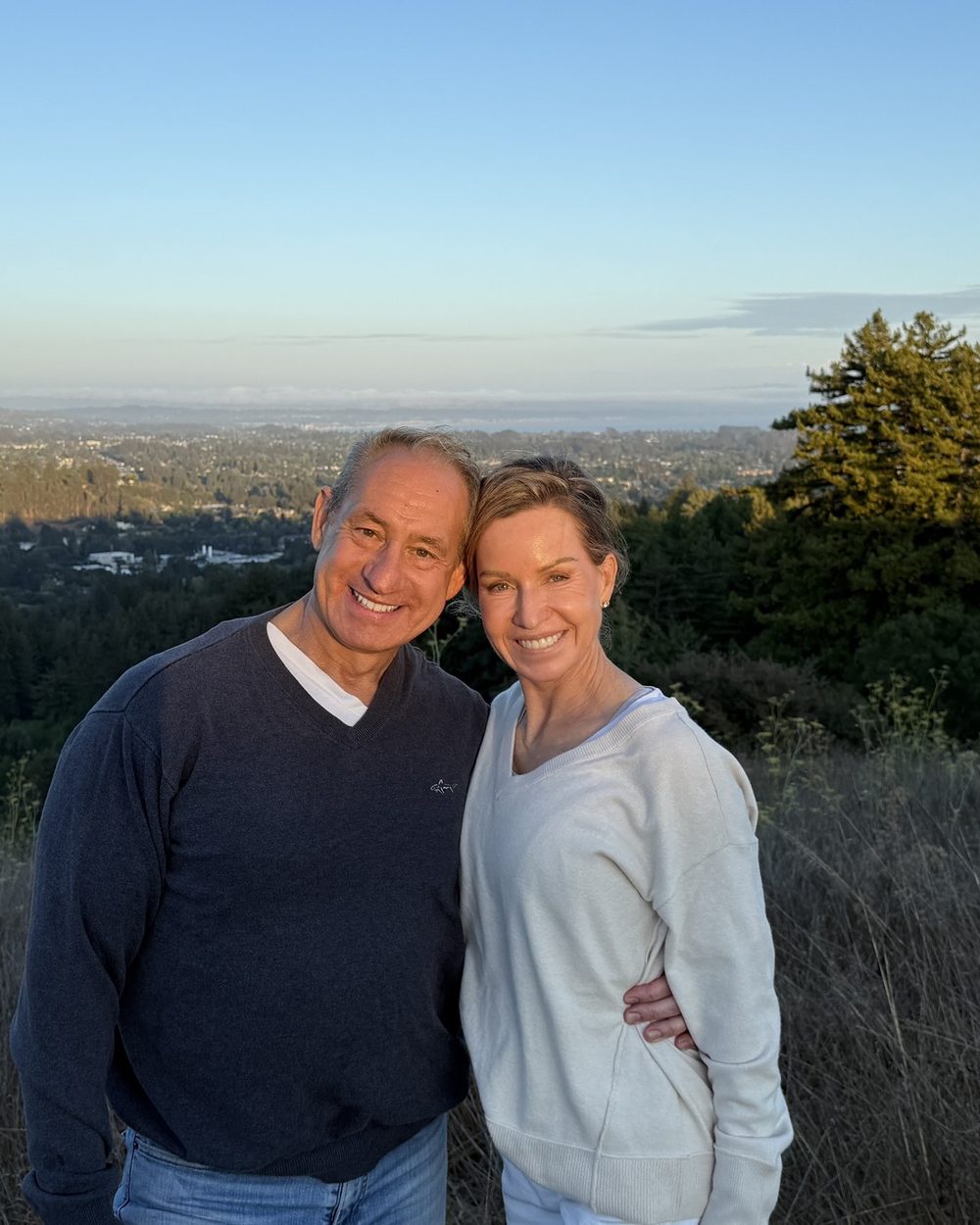 Ben and Loree standing together on a Santa Cruz hilltop at dusk with the valley lights behind them